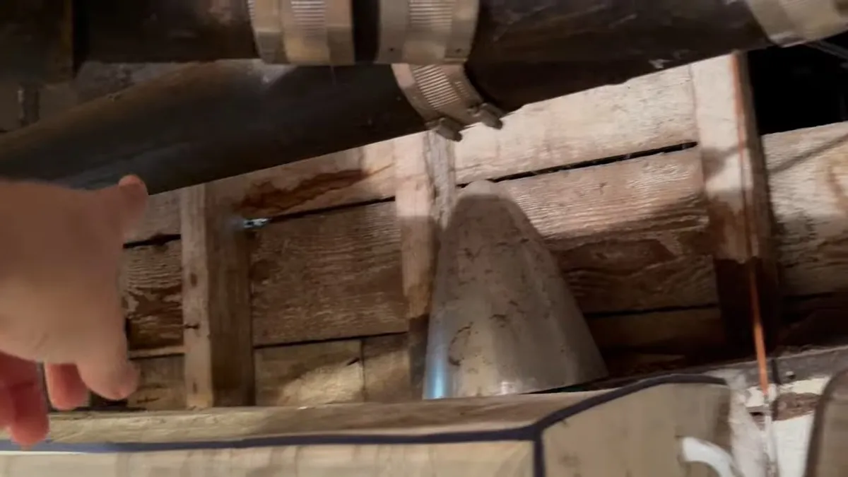 hand points to an aged cast iron line running beneath a wood-framed floor during a plumbing service call in Maricopa, AZ