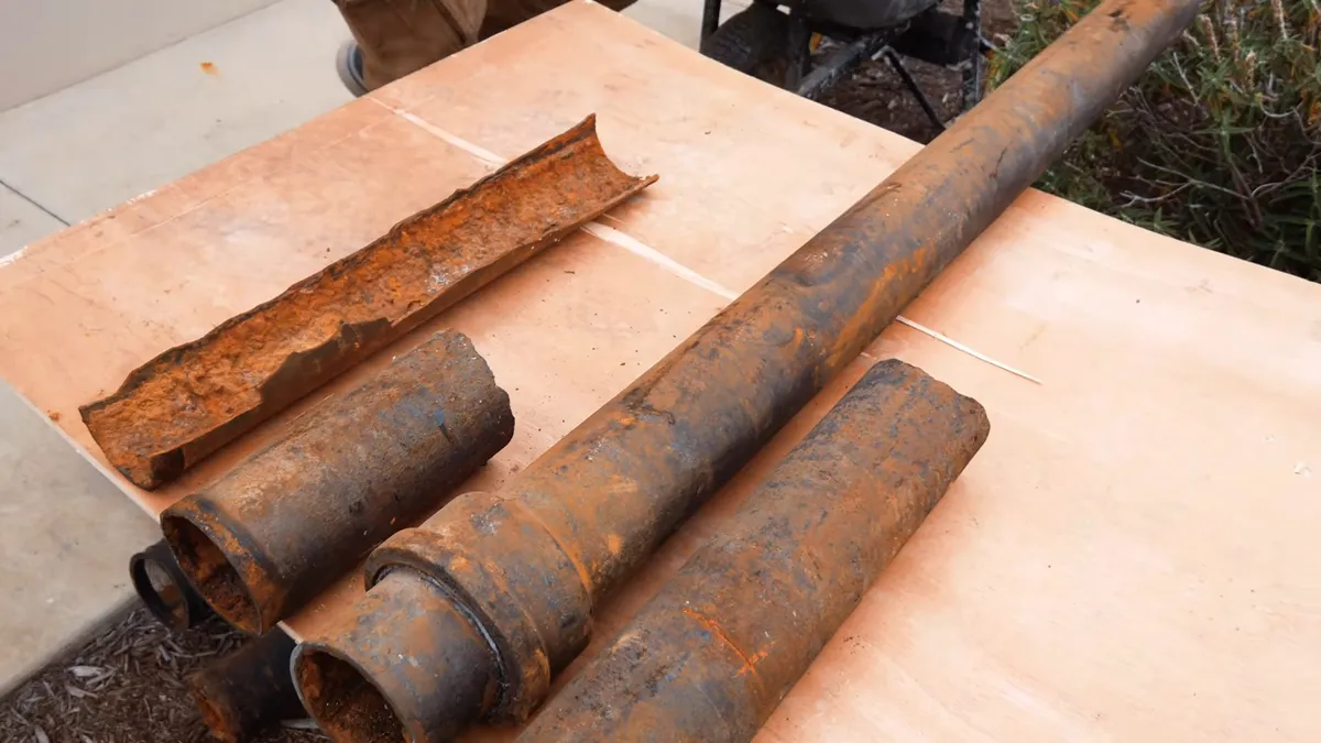 Several removed cast iron pipe sections show severe exterior corrosion on a workbench during a plumbing service call in Maricopa, AZ