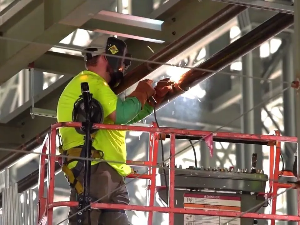 high-visibility worker services overhead piping from a lift inside a warehouse for commercial plumbing in maricopa, az in Maricopa