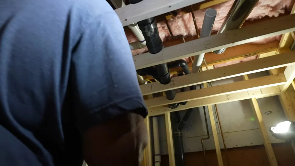 plumber works among copper lines inside an open stud wall during a plumbing service call in Maricopa, AZ