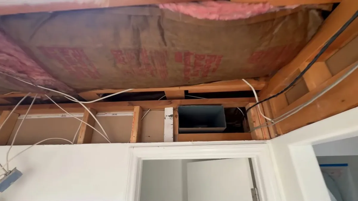 Insulation and framing are exposed above a bathroom before new finishes are installed during a plumbing service call in Maricopa, AZ