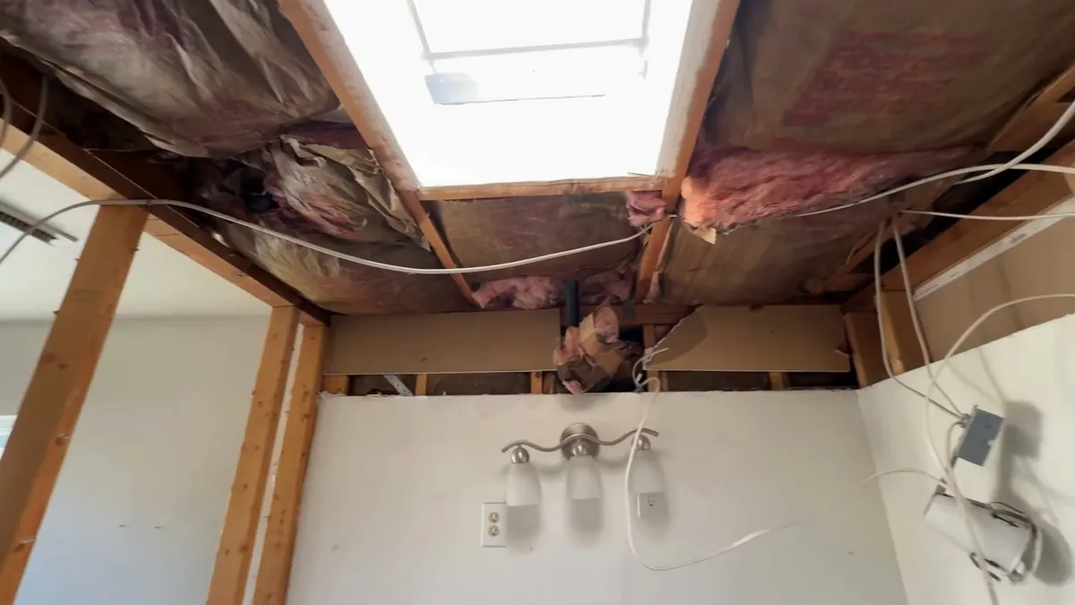 Open ceiling joists reveal insulation, wiring, and plumbing above a bathroom renovation during a plumbing service call in Maricopa, AZ