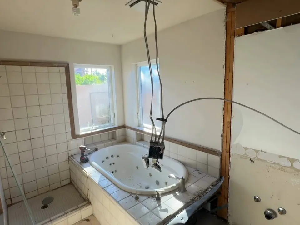 partially demolished bathroom exposes wall studs around the tub and shower area during a plumbing service call in Maricopa, AZ