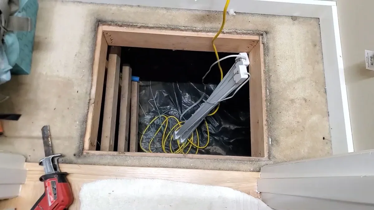 open floor hatch reveals framing and utilities leading into a crawlspace during a plumbing service call in Maricopa, AZ