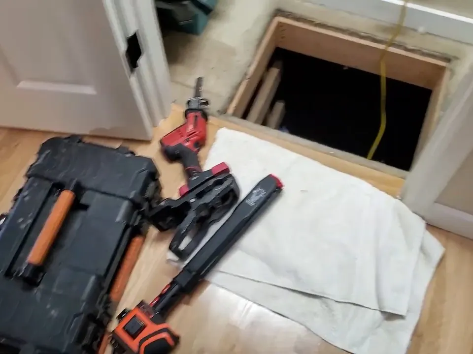 Tools and protective coverings surround an open crawlspace access hatch during a plumbing service call in Maricopa, AZ
