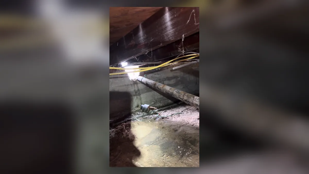 Standing water is visible along a drain line in a dark crawlspace during a plumbing service call in Maricopa, AZ