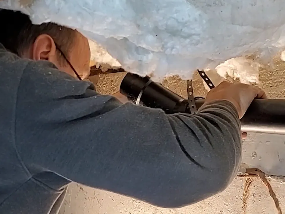 technician makes a pipe connection while working beneath insulation in a crawlspace during a plumbing service call in Maricopa, AZ