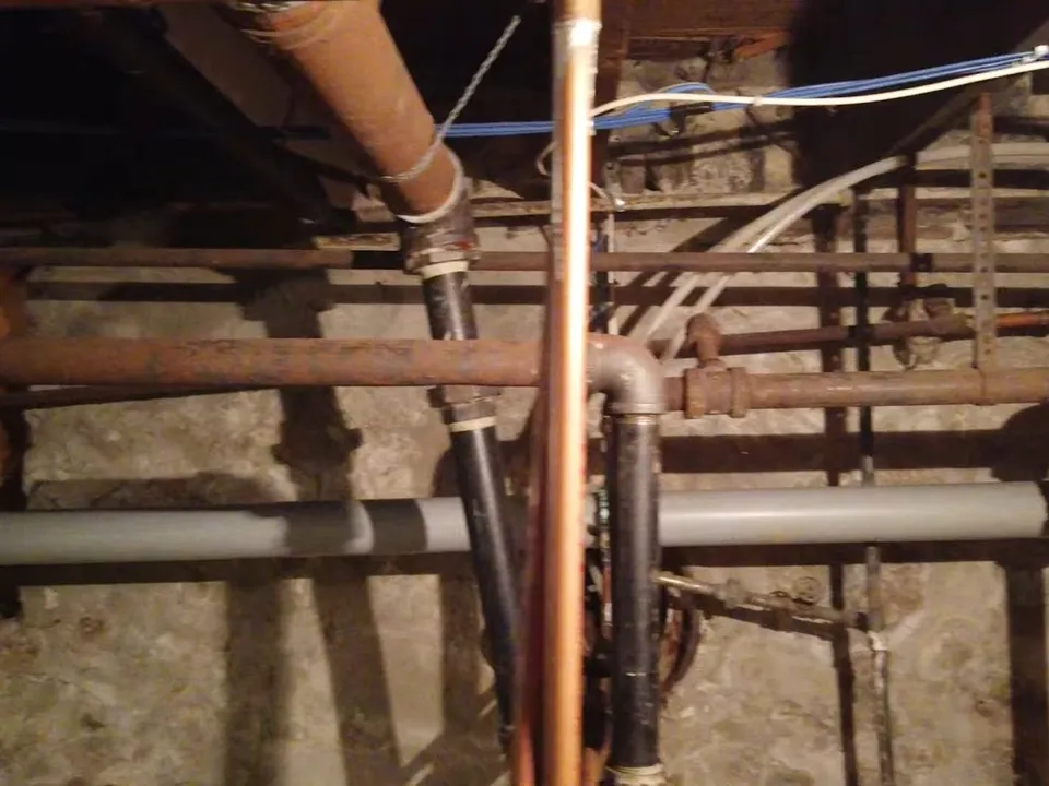 Copper and steel plumbing lines run through an open basement utility area for Maricopa AZ Plumbing Guys