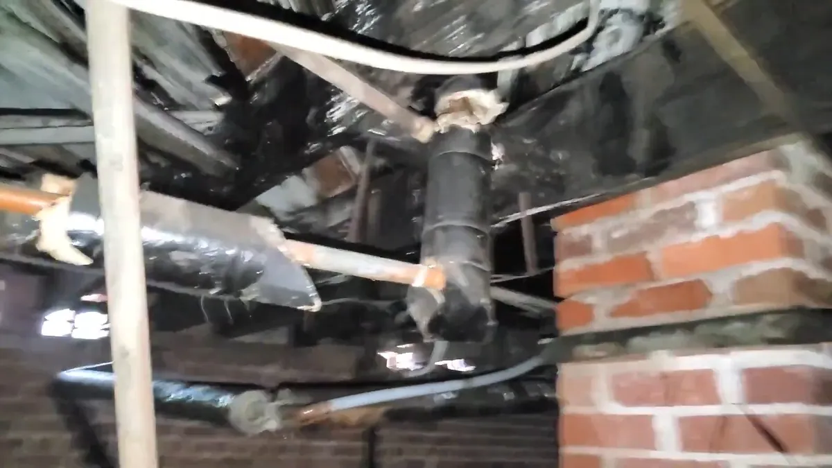 Multiple drain and supply lines run through a brick-walled crawlspace for Maricopa AZ Plumbing Guys
