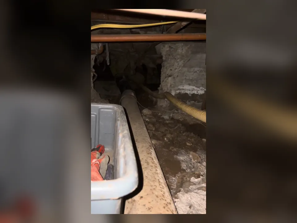 narrow crawlspace contains a long drain line beside a service cart during a plumbing service call in Maricopa, AZ