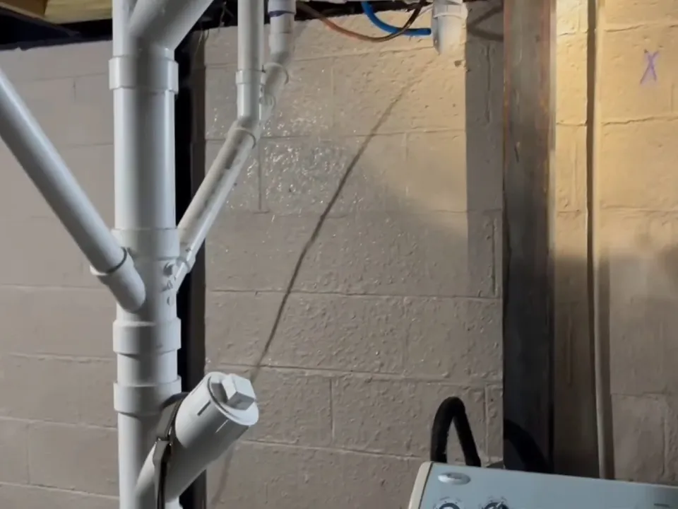 White drain piping and cleanouts run along a basement utility wall during a plumbing service call in Maricopa, AZ