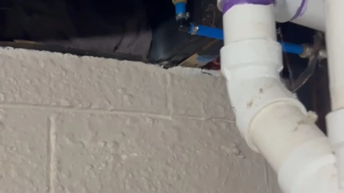 white PVC elbow passes through a masonry wall at a utility connection during a plumbing service call in Maricopa, AZ