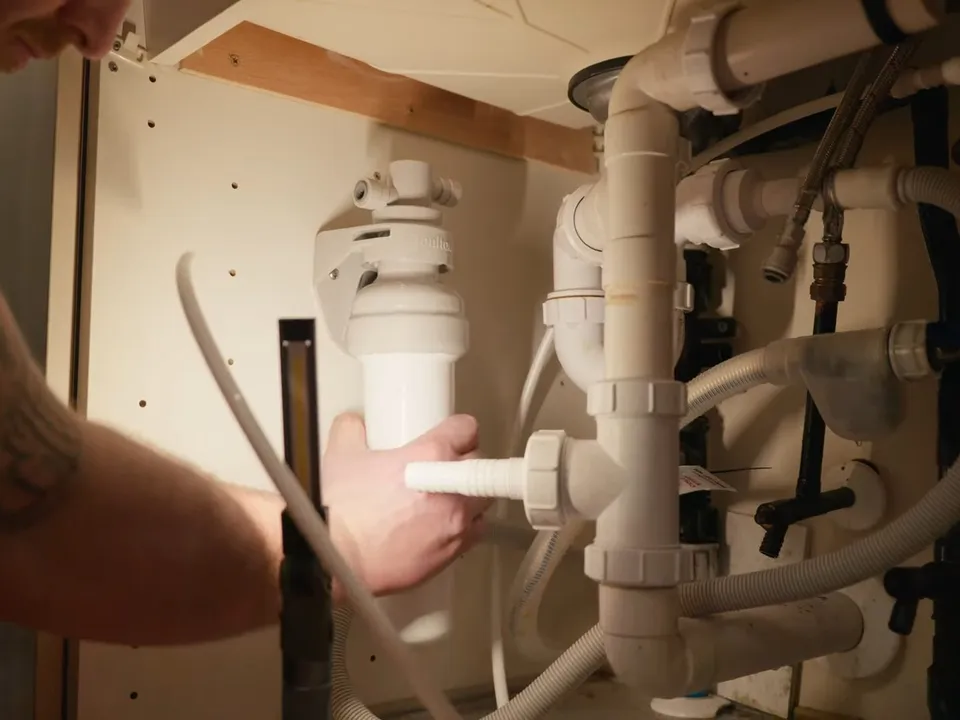 plumber mounts a white under-sink filter housing beside existing drain pipes for reverse osmosis installation in maricopa, az in Maricopa