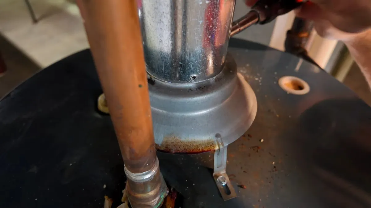 Rust and mineral deposits surround a pipe connection on top of a tank water heater during a plumbing service call in Maricopa, AZ