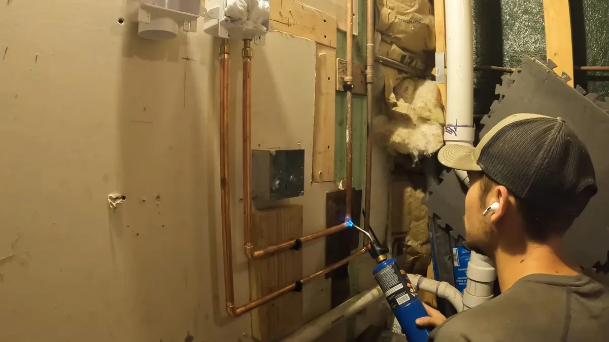 Copper water lines are routed toward a new laundry connection in an unfinished basement during a plumbing service call in Maricopa, AZ