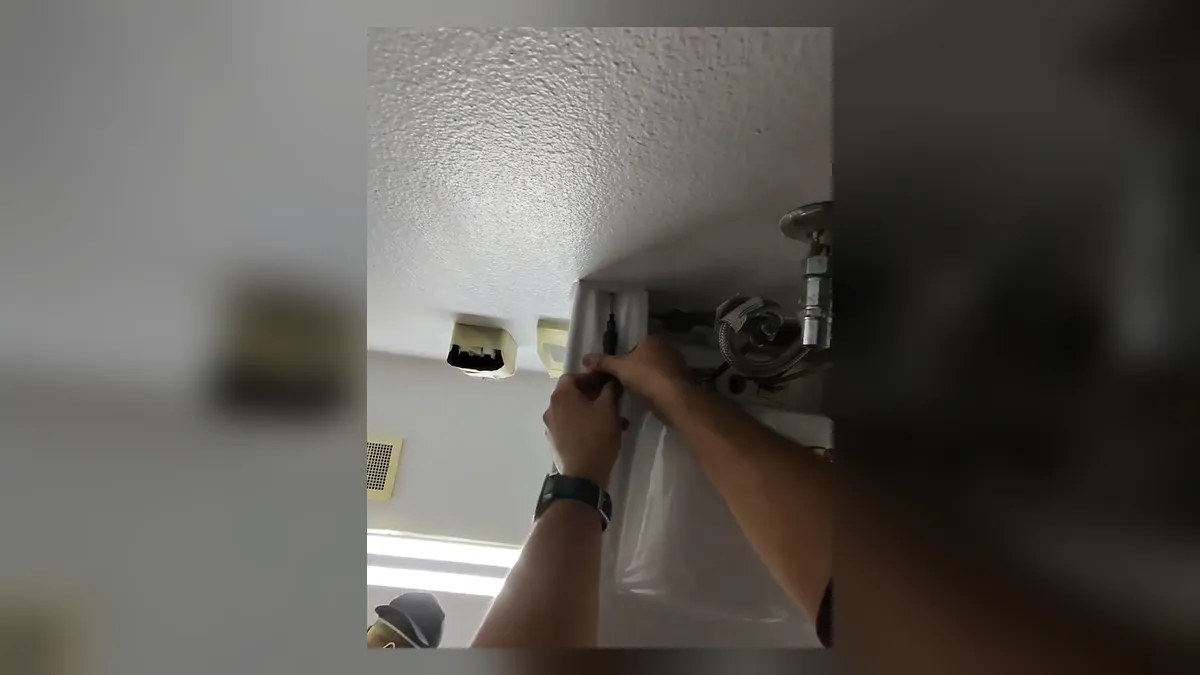plumber connects piping through a ceiling opening above finished cabinets during a plumbing service call in Maricopa, AZ