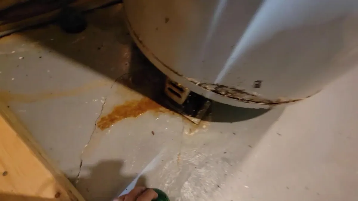 Rust staining is visible around the base seam of an aging tank water heater during a plumbing service call in Maricopa, AZ