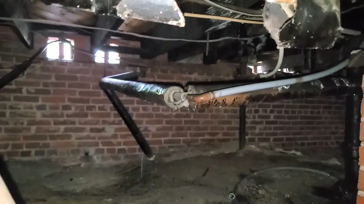 suspended cast iron drain and branch fittings are inspected beneath a building during a plumbing service call in Maricopa, AZ