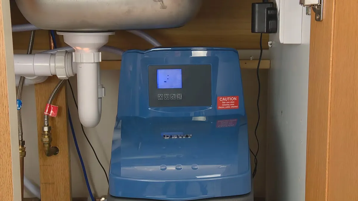 compact blue water-softener control unit is installed beneath a sink during a plumbing service call in Maricopa, AZ