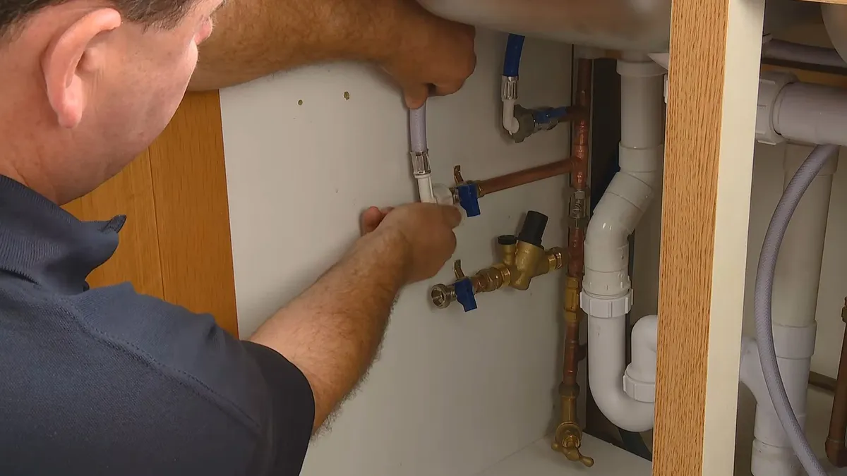 plumber connects a bypass valve beneath a kitchen sink cabinet illustrating Water Softener Sizing for Maricopa Homes: Why 25-35 GPG Requires a Different Calculation